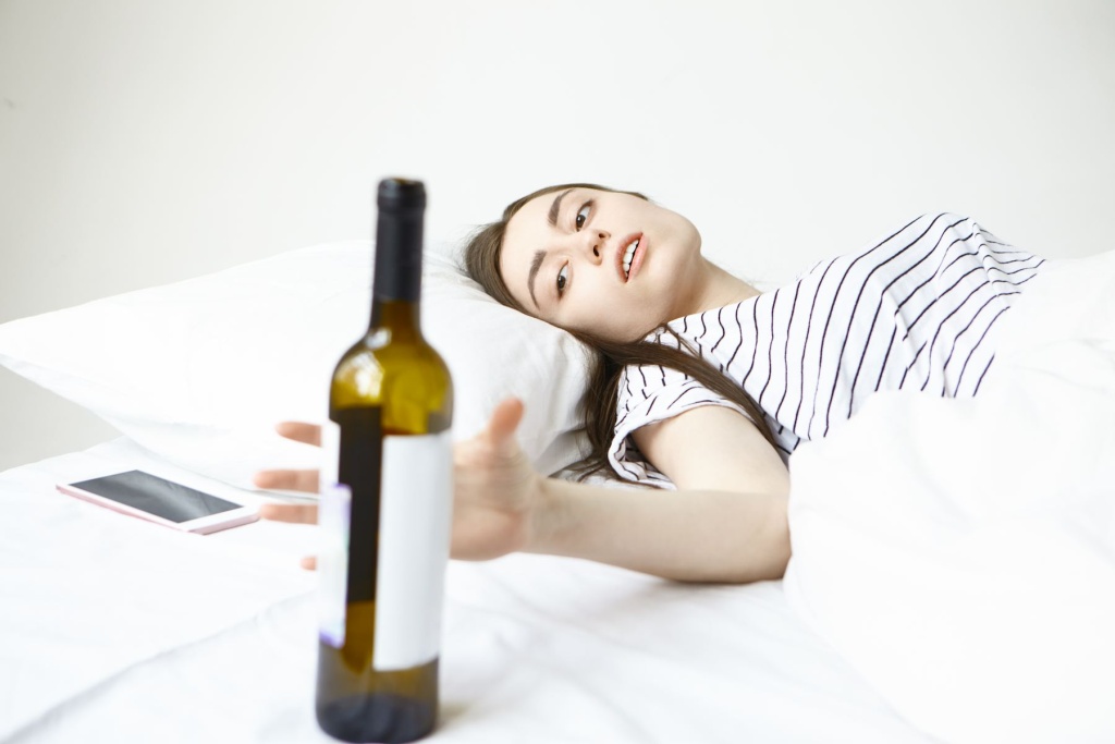 brunette-young-female-suffering-from-terrible-headache-morning-lying-bed-reaching-out-hand-bottle-alcohol (1).jpg